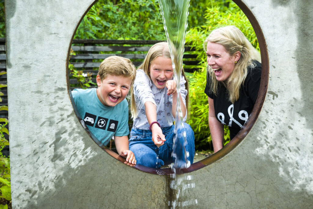 Bilde av to barn og en voksen ved en fontene