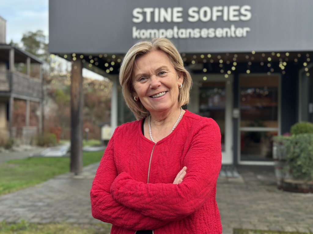 Generalsekretær i Stine Sofies Stiftelse, Ada Sofie Austegard, smiler til kamera foran et julepyntet Stine Sofie Senteret. Foto.